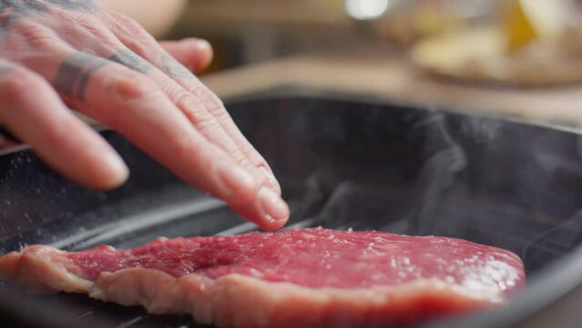 Close up shot of male hand pressing beef steak down while cooking it on hot grill pan