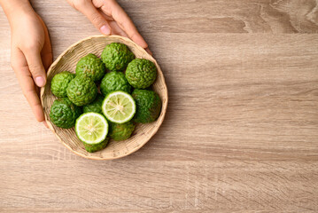 Kaffir lime or bergamot in basket with hand on wooden table, Asian citrus fruit