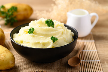 Mashed potato with parsley in black bowl on wooden table