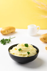 Mashed potato with parsley in black bowl on white and yellow background