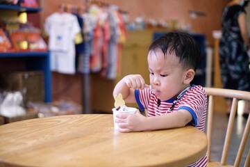 Little Asian kid boy eating ice cream in indoor cafe or restaurant.