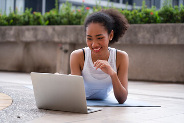 Beautiful black woman using laptop at home while lying down beside the swimming pool after workout to chat with her friends during social distancing with happiness and smiling face