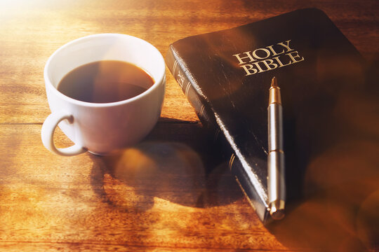 Close up of the holy bible with a pen and a cup of coffee on a wooden table against window light in the morning, Christian concept for bible study or devotional background with copy space for  text