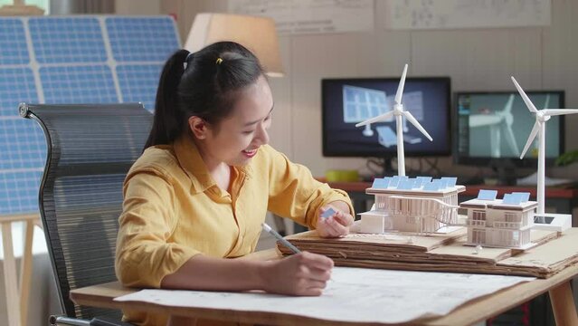 Asian Woman Sketch House With Solar Panel On The Blueprint While Holding It In Hand
