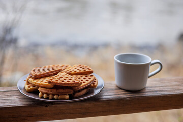 A plate of waffles and a mug of hot coffee stand on the wooden railing of the gazebo. Tourist food. 