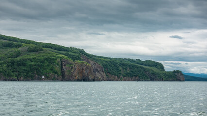 Obraz premium The picturesque coast of Kamchatka against a cloudy sky. Steep rocky shores, green vegetation on the hills. Avacha Bay