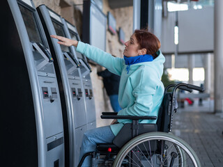 A Caucasian woman in a wheelchair does not reach the self-service checkout at the railway station. Hard-to-reach environment.