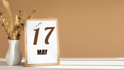 may 17. 17th day of month, calendar date.White vase with dead wood next to cork board with numbers. White-beige background with striped shadow. Concept of day of year, time planner, spring month