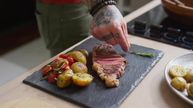 Close up shot of male food stylish putting rosemary twig on slate board with steak, salad and potatoes on side before taking pictures