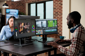 Creative professional videographer in office sitting at multi monitor workstation while editing digital footage. Post production department visual editor improving video quality.
