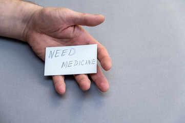 Need medicine. Handwritten gray lettering. Open man's palm with white business card against gray background. Concept of helping people in need. Volunteering.