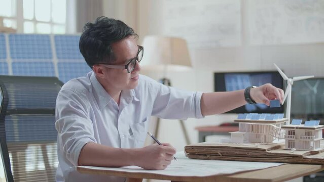 Asian Man Sketch House With Solar Panel On The Blueprint While Holding It In Hand
