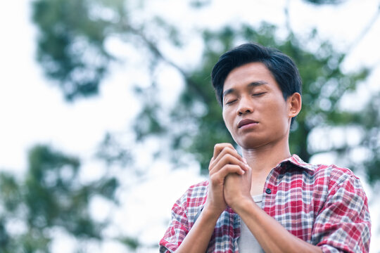 Man holding hands and praying to God with a green tree background. christian prayer concept.