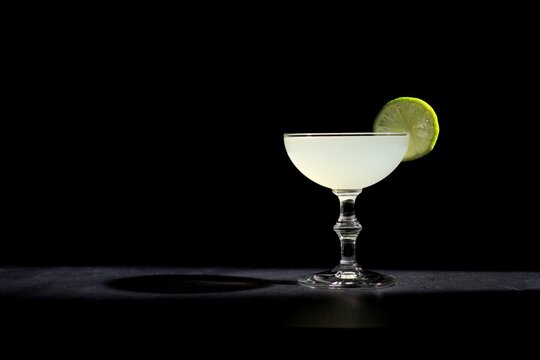 Gimlet gin cocktail, lime garnish agains a black background