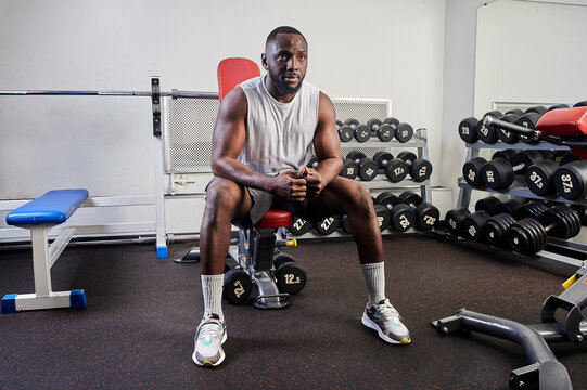 An African-American man is sitting on a bench bench in the gym and resting