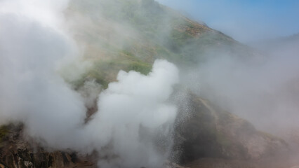 The hillside is shrouded in thick dense steam from an erupting geyser. Poor visibility. The blue sky is visible through the haze. Kamchatka. Valley of Geysers