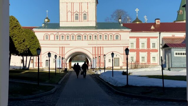 People parishioners enter the Iversky monastery. Static frame. Christian church domes. Spring weather. The sun is shining, blue sky, snow. 4K video.Religious orthodox place. Valday, Russia