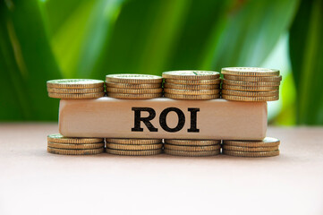 Return on investment text on wooden block with stack of gold coins on blurred background.