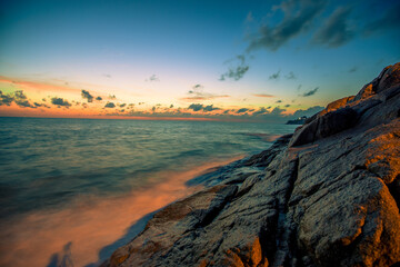 Obraz premium Blurred nature background of the morning sun by the sea, a beautiful golden light, among the trees, rocks and local fishing boats, the beauty of nature during the day.
