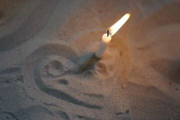 Commemorative burning candle stuck in the sand, surrounded by a heart sign