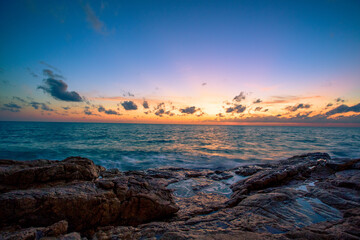 Blurred nature background of the morning sun by the sea, a beautiful golden light, among the trees, rocks and local fishing boats, the beauty of nature during the day.