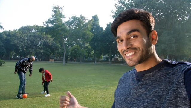 A smiling young man waving his hand and recording a video - picnic  family time  modern-day parenting. An old man and his adorable grandson football in a park - leisure activity  an outdoor sport  ...