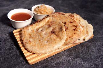 Pupusas on a wooden board with curtido and sauce over a black marble background