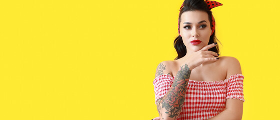 Portrait of beautiful tattooed woman in pin-up style on yellow background with space for text