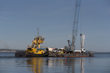 Fototapeta premium PUSHER TUG AND BARGE - A floating platform with crane for hydrotechnical works and concrete mixer trucks on deck