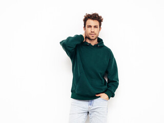 Fototapeta premium Handsome confident hipster model.Sexy unshaven man dressed in summer stylish green hoodie and jeans clothes. Fashion male with curly hairstyle posing in studio. Isolated on white