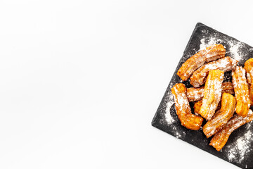 Churros with powdered sugar on black plate. Fat fast food sweets