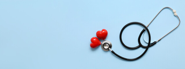 Stethoscope and red hearts on light blue background with space for text. Cardiology concept