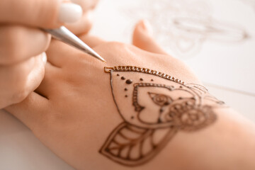Mehndi master drawing henna tattoo on female hand in salon