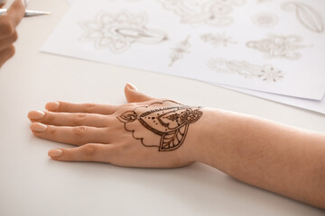 Female hand painted with henna on light background, closeup