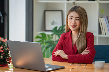 Portrait of young businesswoman using laptop, smiling and looking at camera while sitting at office desk in modern office.