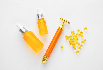 Bottles of oil, vitamin A capsules and facial massage tool on white background