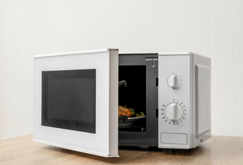 Fototapeta premium Microwave with opened door on wooden table against light background
