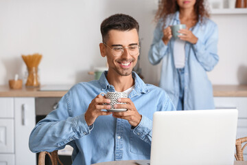 Happy young couple using modern laptop in kitchen