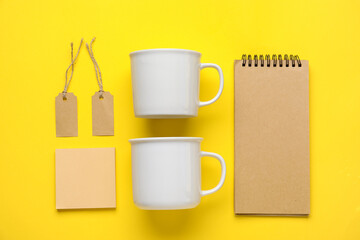 Blank cups, notebook, tags and sticky notes on yellow background