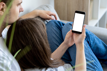 Mobile mockup. Relaxed couple. Online communication. Casual beloved man and woman looking smartphone with blank screen in light room interior.