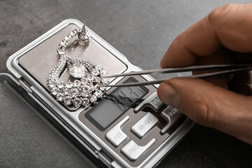 Male hand with tweezers, earring and jewelry scales on black background