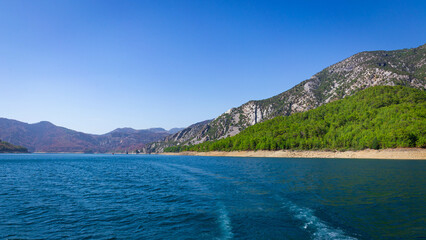View of the green water of the Oymapinar Dam with green trees on the shore