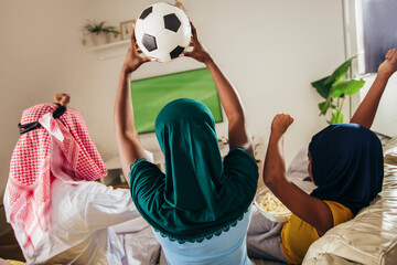 Arab man looking TV at home during a sport event with his family. Watching football game.