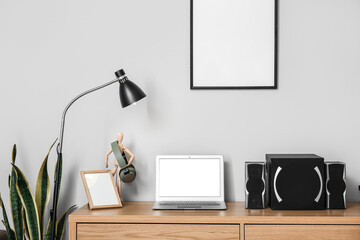 Modern laptop, headphones and speakers on table near light wall
