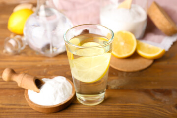 Glass of water and bowl with baking soda on wooden background