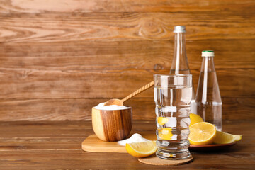 Obraz na płótnie Canvas Glass of water, ripe lemons and baking soda on wooden background
