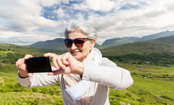 travel, tourism and vacation concept - happy smiling senior woman taking selfie by smartphone over Killarney National Park valley in ireland background