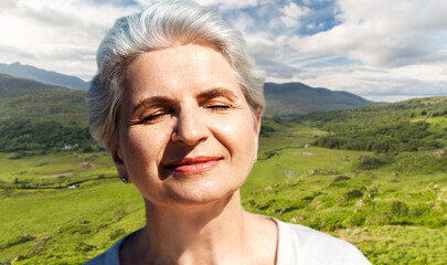 travel, tourism and vacation concept - portrait of happy senior woman enjoying sun over Killarney...