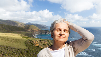 Fototapeta na wymiar travel, tourism and vacation concept - portrait of happy senior woman enjoying sun over atlantic ocean coast in ireland background