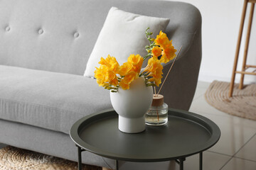 Vase with beautiful flowers and reed diffuser on table near sofa